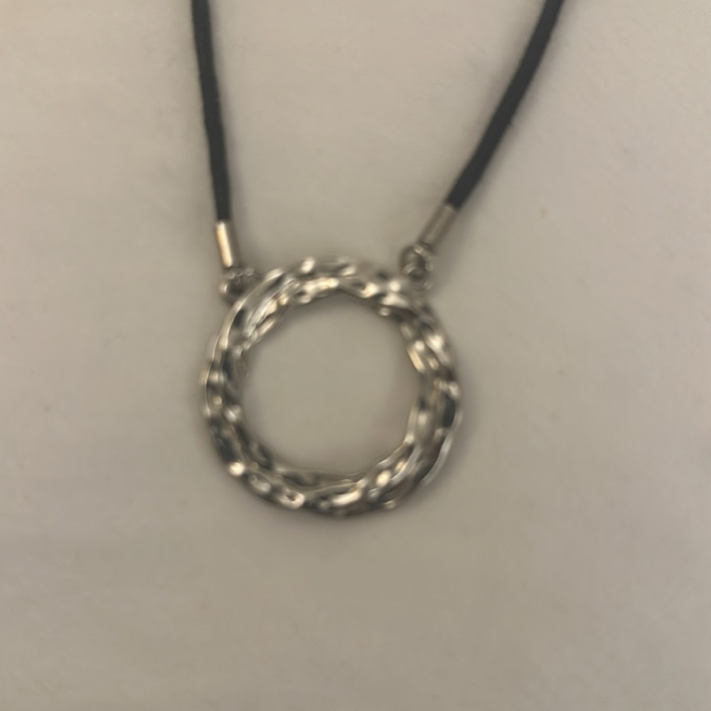 Silver colored pendent with black cord chain.